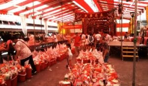 Crowds gathering at a Malaysian temple with rows of red bucket food offerings during the hungry ghost festival celebration.