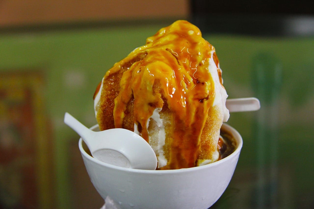 A bowl of Cendol shaved ice dessert topped with coconut milk and a thick, glossy drizzle of Gula Melaka syrup.