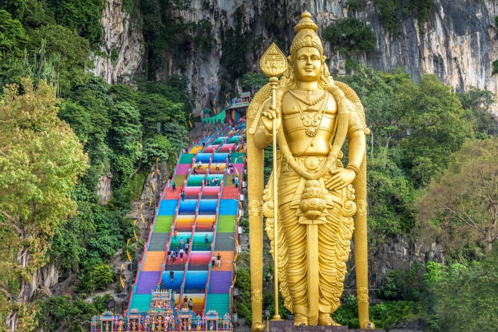 Golden Lord Murugan statue and colorful rainbow stairs at Batu Caves, illustrating the strict dress code Malaysia requires for religious sites.