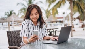 Smiling woman working remotely on a laptop at a tropical resort, representing the relaxed Malaysia digital nomad lifestyle.