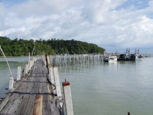 A rustic wooden walkway extending into the calm ocean waters, capturing the atmosphere of the Penang jetty chew and the coastal lifestyle.