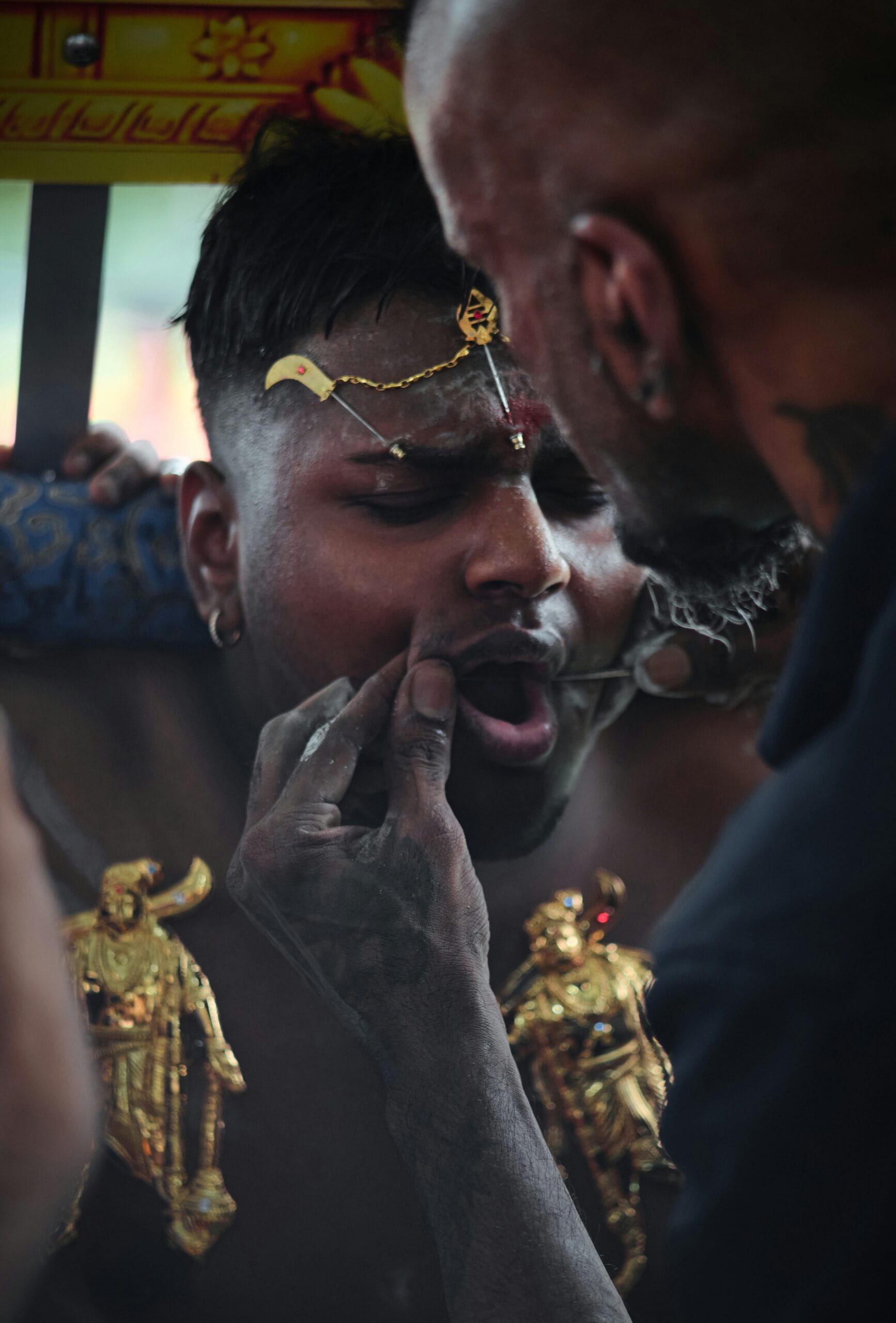 A close-up view of a devotee receiving a ceremonial metal skewer piercing through the cheek during the Thaipusam festival.