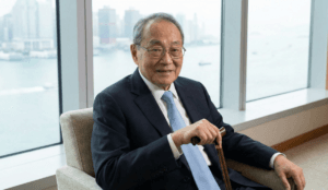 Malaysian businessman and billionaire Robert Kuok smiling while seated in an office overlooking a coastal city skyline.