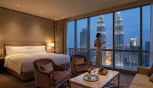 Interior of a luxury suite in the best 5 star hotel in Kuala Lumpur featuring floor-to-ceiling windows with a direct view of the Petronas Twin Towers at dusk.