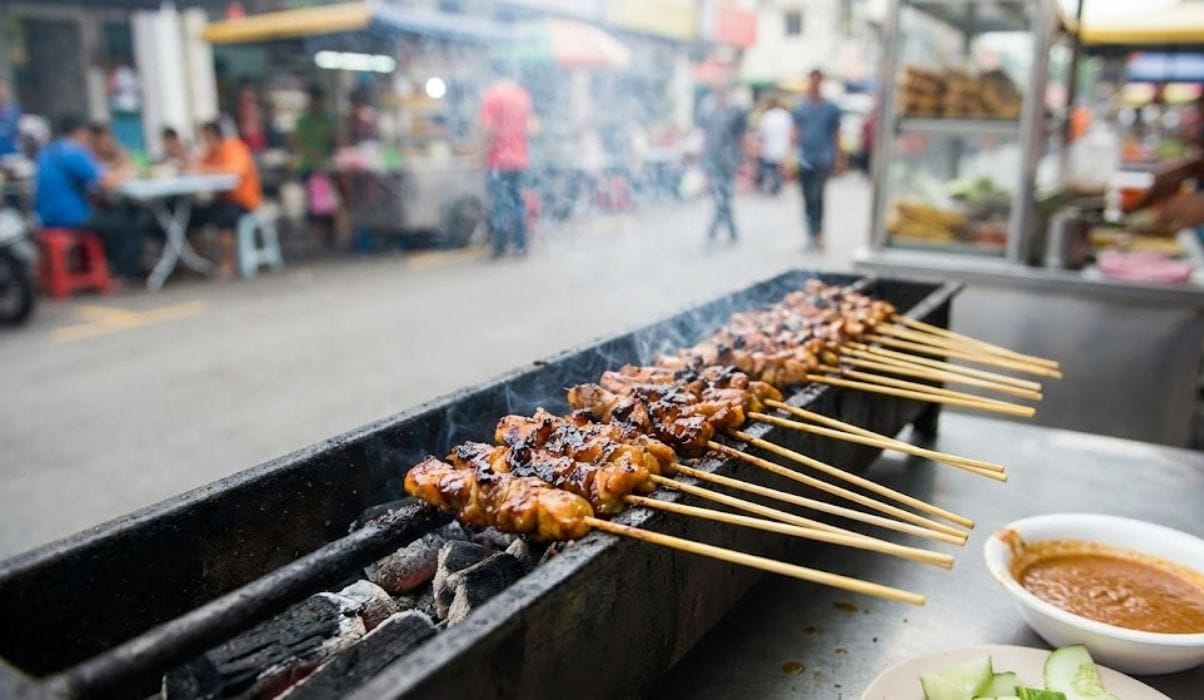 Close-up of Malaysian chicken satay skewers being grilled on a charcoal barbecue at a street food stall in Kuala Lumpur.