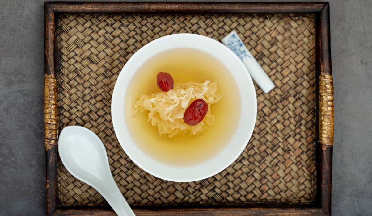 Top-down view of a white bowl containing traditional tonic with red dates on a woven wooden tray, illustrating bird's nest soup benefits.