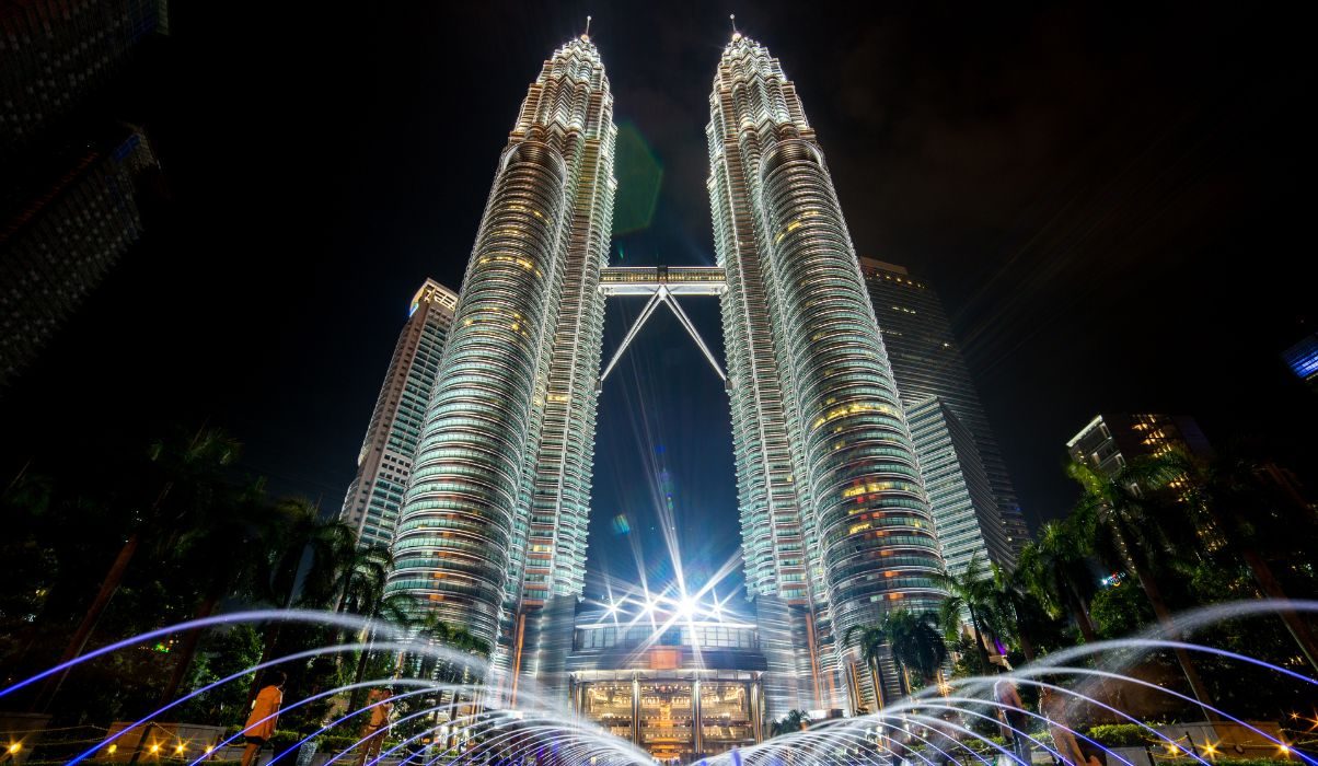 The Petronas Twin Towers in Kuala Lumpur at night with illuminated fountains in the foreground.