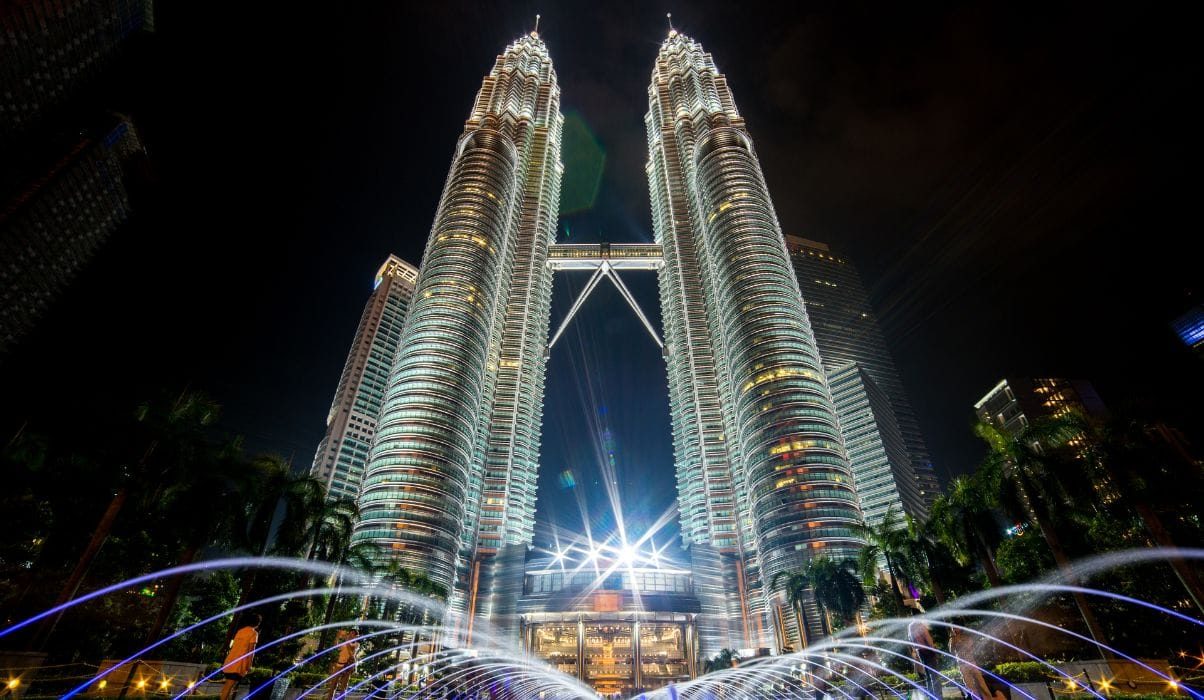 The Petronas Twin Towers in Kuala Lumpur at night with illuminated fountains in the foreground.