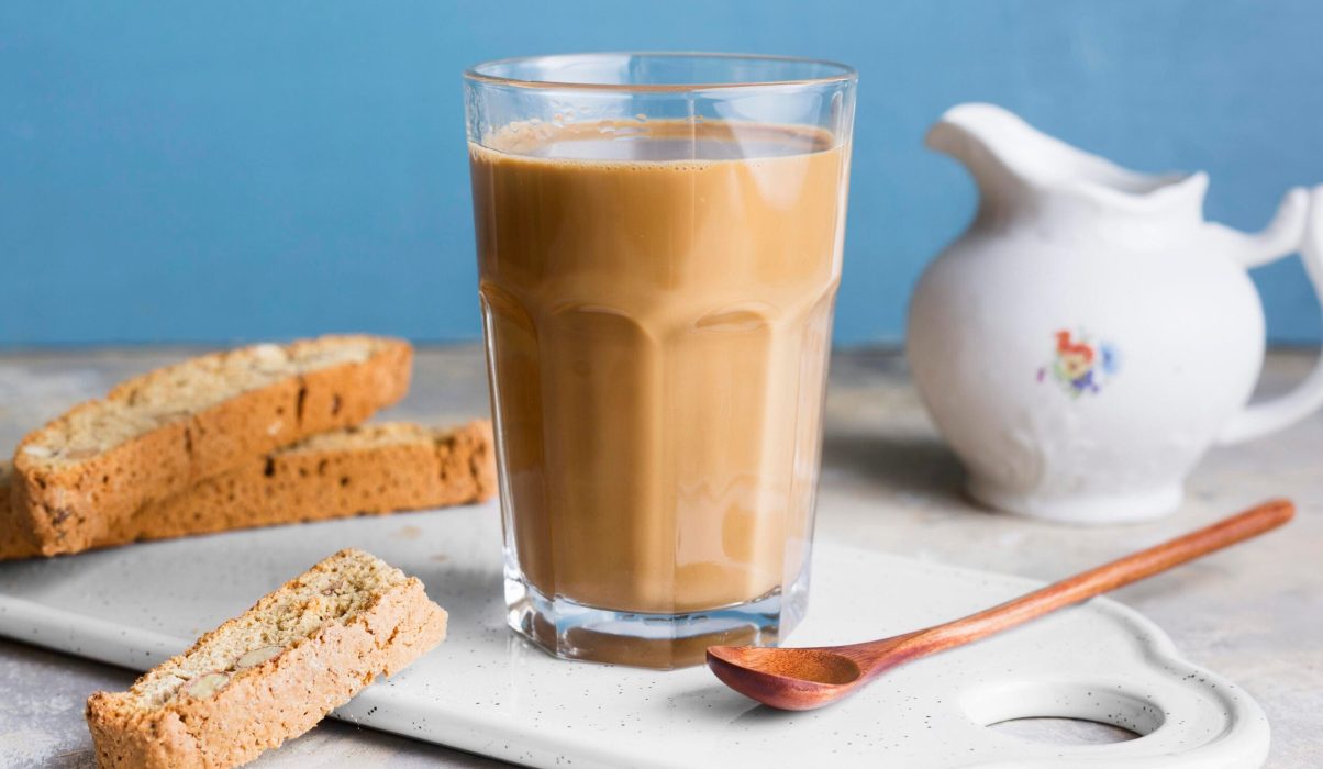 A glass of teh tarik served with crunchy biscuits for dipping, representing modern Malaysian breakfast or minum petang culture.